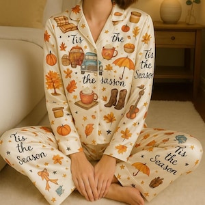 Peut inclure: Ensemble de pyjama crème avec un imprimé sur le thème de l'automne. Le haut à manches longues et le pantalon présentent des citrouilles, des feuilles, des tasses à café et le texte "Tis the Season". L'ensemble comprend une chemise boutonnée et un pantalon à taille élastique.