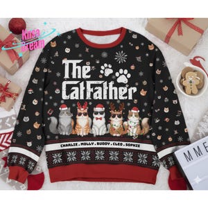 May include: Black crew neck sweater with the text "The Catfather" and images of cats wearing sunglasses and holiday accessories. The sweater has a red collar, cuffs, and bottom hem with a snowflake pattern. The names "Charlie, Molly, Buddy, Cleo, Sophie" are printed at the bottom.