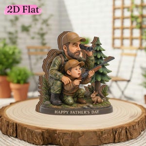 Op de afbeelding: Een gedetailleerd beeldje dat een vader en kind toont die aan het jagen zijn, met de tekst "HAPPY FATHER'S DAY" aan de basis. De vader gebruikt een verrekijker, terwijl het kind een geweer richt. De scène omvat een klein konijn en een dennenboom.