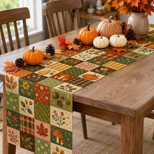May include: A rectangular table runner featuring a patchwork pattern of autumn-themed squares. The design includes illustrations of orange pumpkins, red mushrooms, brown acorns, yellow flowers, green leaves, and plaid textures in shades of orange, green, and brown.