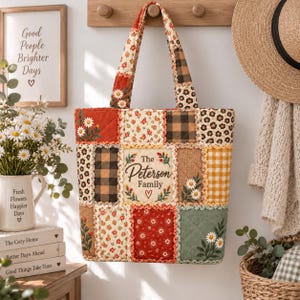Può includere: Una borsa tote patchwork trapuntata con vari quadrati di tessuto in motivi floreali, a quadri e vichy. Il pannello centrale mostra il testo The Peterson Family con un'icona a forma di cuore. La borsa ha due manici e un bordo in pizzo.