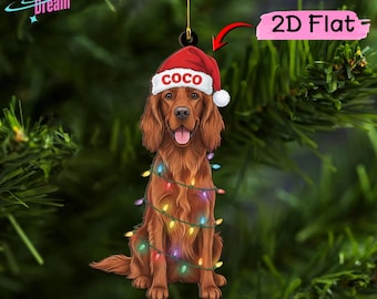 May include: A flat, two-dimensional Christmas tree ornament featuring a brown Irish Setter dog wearing a red Santa hat with the name COCO printed in white letters. The dog is wrapped in a string of colorful, glowing holiday lights.