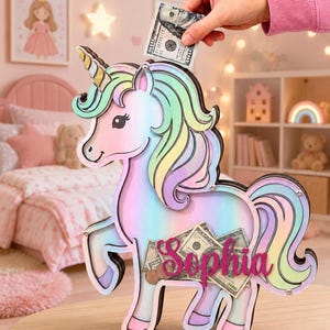 Pu&ograve; includere: Un salvadanaio a forma di unicorno dai colori pastello, con criniera e coda arcobaleno. C'&egrave; il nome "Sophia". Una mano inserisce una banconota da 100 dollari. Il salvadanaio &egrave; in legno.