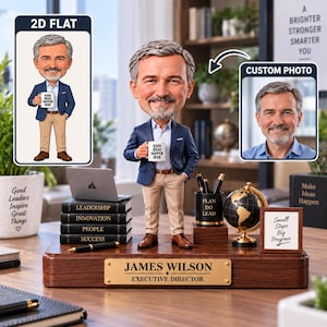 Peut inclure: Une figurine bobblehead personnalisée d'un homme aux cheveux gris et à la barbe, portant un blazer bleu et un pantalon beige, tenant une tasse avec l'inscription GOOD IDEAS HAPPEN HERE. Elle repose sur un socle en bois avec une plaque JAMES WILSON.
