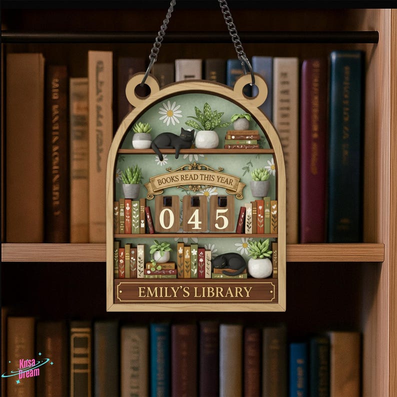 May include: Wooden bookshelf-shaped sign with a chain for hanging. The sign features a miniature library scene with books, plants, and a black cat. Text on the sign includes "BOOKS READ THIS YEAR", "045", and "EMILY'S LIBRARY".