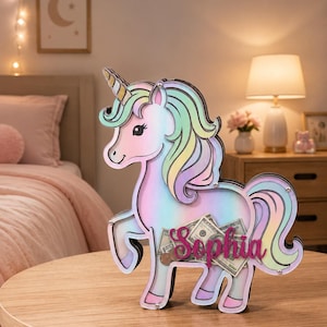 Pu&ograve; includere: Un salvadanaio a forma di unicorno dai colori pastello, con criniera e coda arcobaleno. Il salvadanaio contiene denaro e ha il nome "Sophia". Il salvadanaio &egrave; fatto di legno e poggia su un tavolo di legno.