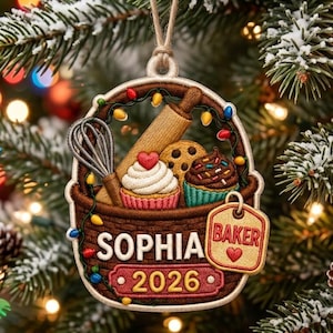 Könnte beinhalten: Ein brauner, geflochtener Korb-Anhänger mit Nudelholz, Schneebesen, Cupcake und Schokoladenkeks. Der Text lautet Sophia, Baker und 2026. Eine bunte Lichterkette windet sich um den Korb, der an einer Schnur aufgehängt ist und festlich gestaltet wurde.