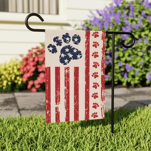 Peut inclure: Un drapeau de jardin patriotique avec un motif de drapeau américain vieilli, avec une empreinte de patte et des étoiles. Le drapeau a des rayures rouges et blanches, une empreinte de patte bleue avec des étoiles blanches et des empreintes de pattes rouges.