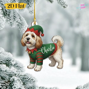 Op de afbeelding: Een kerstversiering met een hond verkleed als elf. De hond draagt een groen en rood elf-outfit met de naam "Charlie" op de trui. De versiering hangt aan een gouden draad. De tekst "2D Flat" staat linksboven.