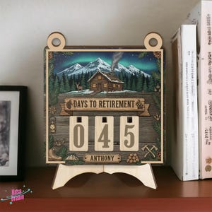 Puede incluir: Calendario de cuenta regresiva de jubilación de madera con una escena de cabaña, montañas y el texto "DAYS TO RETIREMENT". Los números muestran "045" días restantes. El nombre "ANTHONY" está debajo. El calendario está sobre un soporte de madera.
