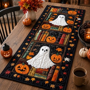Peut inclure: Un chemin de table rectangulaire en tissu avec un fond noir, orné d'un motif matelassé de livres empilés, de citrouilles d'Halloween orange et de fantômes blancs. La bordure est décorée de petites feuilles d'automne orange et rouges.