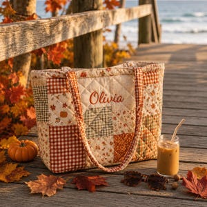 Könnte beinhalten: Eine gesteppte Tragetasche mit einem Patchwork-Design aus herbstlichen Stoffen, darunter orange-weißes Vichy-Karo, grünes Schottenkaro und Kürbis-Motive. Der Name Olivia ist in orangefarbener Schreibschrift auf der Vorderseite eingestickt.