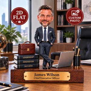 Può includere: Una statuetta bobblehead personalizzata di un uomo in abito scuro su una base in legno con una targa dorata che riporta la scritta James Wilson Chief Executive Officer. La base presenta tre libri intitolati Leadership, Innovation e Success.