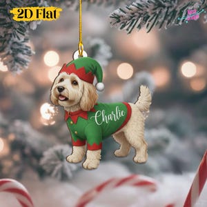 Peut inclure: Ornement de Noël plat 2D représentant un chien déguisé en elfe. Le chien porte un costume vert avec des bordures rouges et un chapeau assorti. Le nom "Charlie" est écrit sur la chemise du chien.