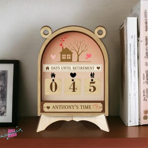 May include: A wooden retirement countdown calendar with a light brown frame and a pink background. The calendar displays "DAYS UNTIL RETIREMENT" and shows "045" days remaining. The bottom of the calendar reads "ANTHONY'S TIME".