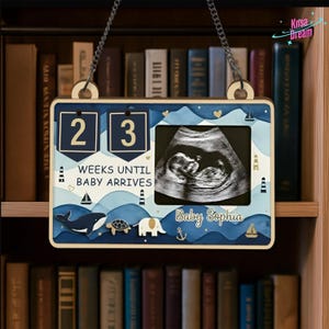 May include: Wooden pregnancy countdown sign with a nautical theme. The sign displays "23 WEEKS UNTIL BABY ARRIVES" and includes an ultrasound image. Decorative elements include a whale, turtle, elephant, and sailboats. The baby's name, Sophia, is also displayed.