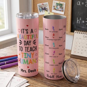 May include: A pink 20oz stainless steel tumbler with a clear lid. One side features the text "IT'S A BEAUTIFUL DAY TO TEACH TINY HUMANS" and "Mrs. Davis". The other side shows a water intake tracker with hourly markers from 8am to 7pm.