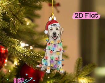 May include: A 2D flat hanging ornament featuring a light-colored Labrador retriever wearing a red and white Santa hat with the name Teddy printed on the brim. The dog is wrapped in a string of colorful Christmas lights and hangs by a gold cord.