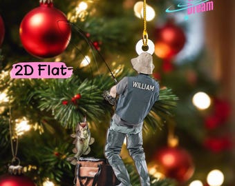 May include: A 2D flat hanging ornament featuring a person wearing a tan bucket hat, a grey vest with the name WILLIAM printed on the back, and grey waders. The person holds a fishing rod with a fish on the line above a brown tackle box.