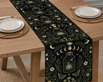 May include: A black table runner featuring a repeating pattern of glass jars containing crystals, surrounded by gold and green illustrations of moon phases, stars, moths, ferns, and small mushrooms. The design is printed on a dark fabric surface.