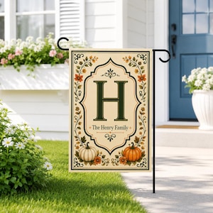 Puede incluir: Una bandera de jardín rectangular con fondo crema y borde verde oscuro. El centro muestra una letra H grande en verde oscuro sobre el texto The Henry Family. El diseño incluye calabazas naranjas y blancas y follaje de otoño.