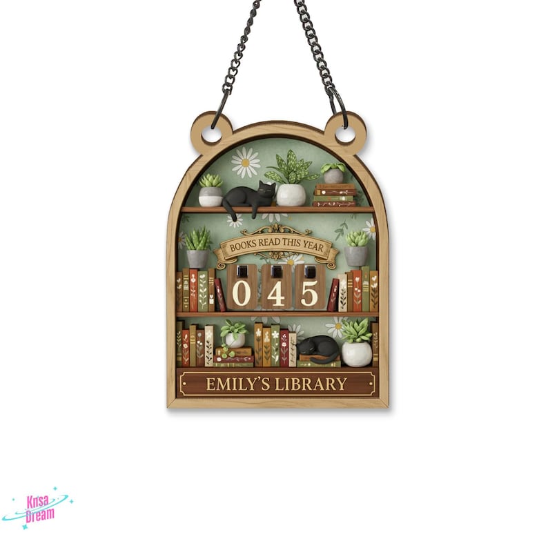 May include: Wooden bookshelf-shaped wall hanging with a chain for hanging. The shelves display miniature books, plants, and sleeping black cats. The text "BOOKS READ THIS YEAR" and "EMILY'S LIBRARY" are visible. The counter reads "045".