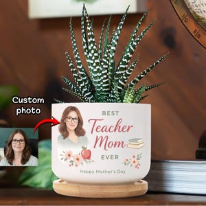 Könnte beinhalten: Ein weißer Keramik-Blumentopf mit einer Sukkulentenpflanze. Der Topf hat ein individuelles Foto einer Frau und den Text "Best Teacher Mom Ever" mit einem Apfel und Blumen. Er steht auf einem Holzsockel. "Happy Mother's Day" steht unten.