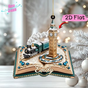 May include: A flat 2D hanging ornament featuring an open book with gold-trimmed pages, a black and teal steam train with snow, and a tall clock tower. The name Emily is printed in white script on the book. It includes a gold hanging string.