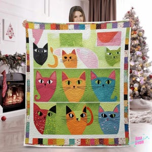 Könnte beinhalten: Eine farbenfrohe Steppdecke mit einem sich wiederholenden Muster stilisierter Katzenköpfe in verschiedenen Farben, darunter Schwarz, Orange, Rosa und Blau, vor einem grünen Hintergrund. Die Steppdecke hat einen Patchwork-Rand mit einer Vielzahl von Mustern und Farben. Die Steppdecke wird von einer Person gehalten.