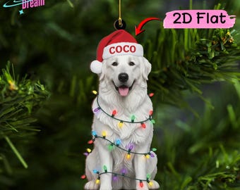 May include: A flat, two-dimensional Christmas tree ornament shaped like a white dog wearing a red Santa hat with the name COCO printed in red letters. The dog is wrapped in a string of colorful, glowing Christmas lights against a green background.