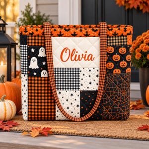 May include: A quilted tote bag featuring a patchwork design with Halloween motifs including ghosts, jack-o'-lanterns, spiderwebs, and black and orange buffalo plaid. The center panel is cream-colored with the name Olivia printed in orange script.