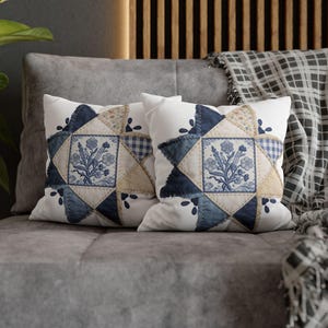 May include: Two white throw pillows with a patchwork design. Each pillow features a central square with a blue floral pattern, surrounded by blue denim, tan, and gingham fabric. The pillows rest on a gray sofa.