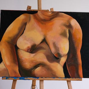 May include: Oil painting of a torso on canvas, displayed on a wooden easel. The artwork depicts a nude figure against a black background. The skin tones are rendered in shades of orange, yellow, and pink.