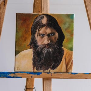 Può includere: Dipinto a olio su tela di un uomo con lunga barba e capelli neri, e penetranti occhi blu. L'uomo indossa una camicia gialla. Lo sfondo è una miscela di verde e marrone.