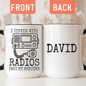 May include: A white ceramic mug with a black handle and interior. The front features a black line drawing of a radio with the text I TINKER WITH RADIOS PAST MY BEDTIME. The back displays the name DAVID in bold black capital letters.
