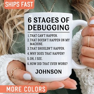 May include: A white ceramic mug featuring the black text 6 STAGES OF DEBUGGING followed by a numbered list of six humorous statements about programming and the name JOHNSON printed in bold capital letters at the bottom of the mug surface.