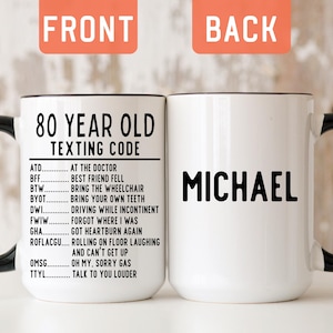 May include: A white ceramic mug with a black handle and rim. The front features the black text 80 YEAR OLD TEXTING CODE followed by a list of humorous abbreviations and their meanings. The back displays the name MICHAEL in bold black letters.