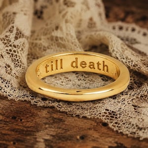 May include: A gold-toned metal ring with a smooth, polished exterior surface. The inner band of the ring features the engraved text 'till death' in a clear, sans-serif font, visible along the interior circumference of the circular band.