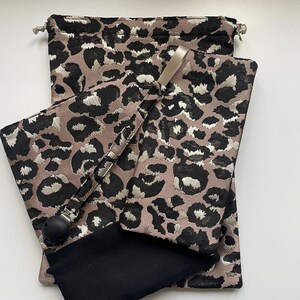 Peut inclure: Un ensemble d'accessoires pour bébé avec un motif léopard noir, beige et crème. L'ensemble comprend un sac à cordon, un porte-sucette et une petite pochette avec un accent noir.