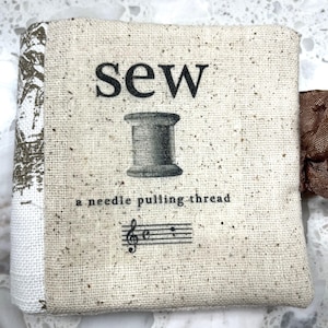 May include: A square, fabric-covered sewing kit with the word "sew" in large black letters. Below the word is an illustration of a spool of thread. The text "a needle pulling thread" is below the spool, with musical notes at the bottom.