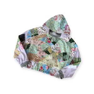 May include: A patchwork hoodie with a mix of floral and patterned fabrics in various colors, including pink, blue, green, and yellow. The hoodie has a drawstring, a pocket, and gray ribbed cuffs and hem.