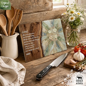 May include: A rectangular glass cutting board featuring a natural wood grain edge on the left and a floral cross design on the right. The text reads: Lord, Bless her with peace and strength today. Fill her home with Your love and her heart with Your joy. Guide her steps, calm her worries, and remind her how deeply she is loved. AMEN.