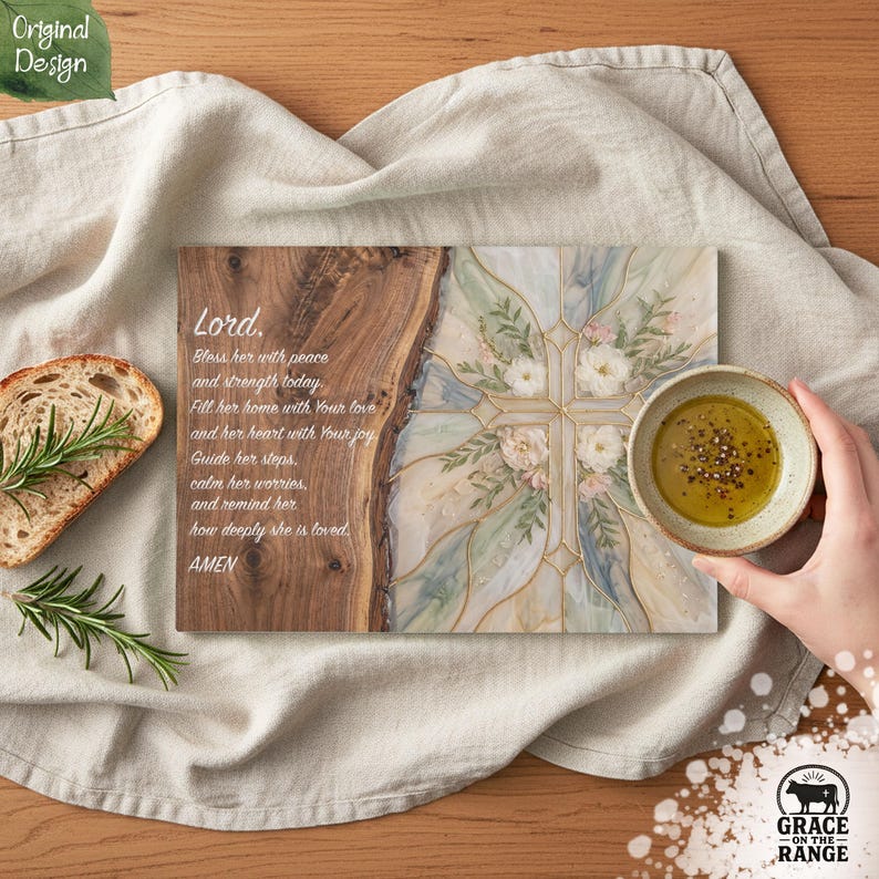 May include: A rectangular wooden serving board featuring a natural live edge on the left and a decorative cross design with floral accents on the right. The board includes the printed text: Lord, Bless her with peace and strength today. Fill her home with Your love and her heart with Your joy. Guide her steps, calm her worries, and remind her how deeply she is loved. AMEN.