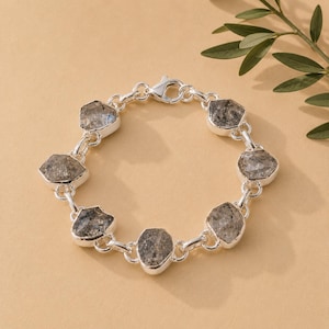 Puede incluir: Una pulsera de cadena de plata con seis piedras grises irregulares y facetadas engastadas en biseles de plata pulida. La pulsera está construida con eslabones circulares de plata que conectan cada engaste y tiene un cierre de mosquetón.