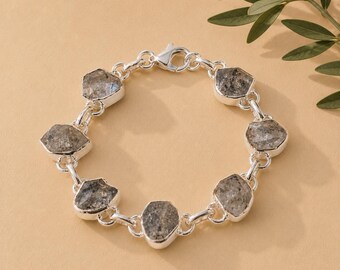 May include: A silver chain bracelet featuring six irregular, faceted gray stones set in polished silver bezels. The bracelet is constructed with circular silver links connecting each stone setting and includes a silver lobster claw clasp closure.