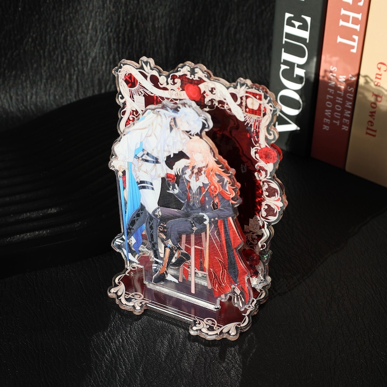 May include: A decorative acrylic stand featuring a romantic illustration of two figures in an ornate frame. The figures are depicted in shades of white, blue, and red, with intricate details and a vintage aesthetic. The stand is clear with a decorative border.