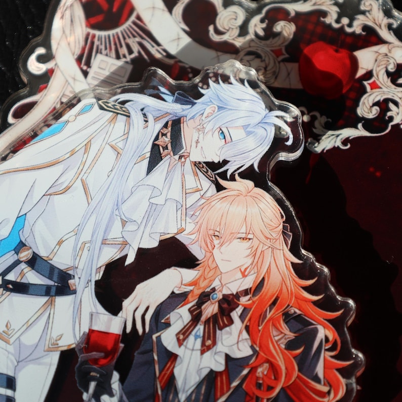 May include: A clear acrylic charm featuring two anime-style male figures. One has long white hair and wears a white and gold outfit. The other has long orange hair and wears a black and red outfit, holding a glass of red liquid. The background is dark red.