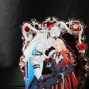 May include: Acrylic stand featuring two anime-style characters in ornate outfits. One character has white hair and a white and blue outfit, while the other has long orange hair and a black and red ensemble. The background is a decorative red and white design.