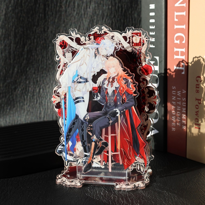 May include: A clear acrylic stand featuring two anime-style figures in elaborate outfits. One figure is seated, holding a glass of red liquid, while the other stands. The stand has a decorative red and white border with floral accents.
