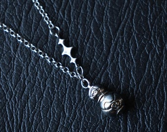 May include: A silver-toned metal necklace featuring a delicate chain with a four-pointed star charm and a small, rounded pendant shaped like a stylized figure with engraved facial features and a smooth, reflective surface finish.